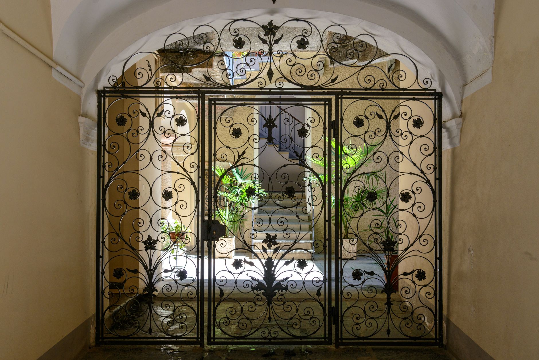 Elegant iron gate with intricate designs opening into a sunlit corridor with plants in Austin, TX