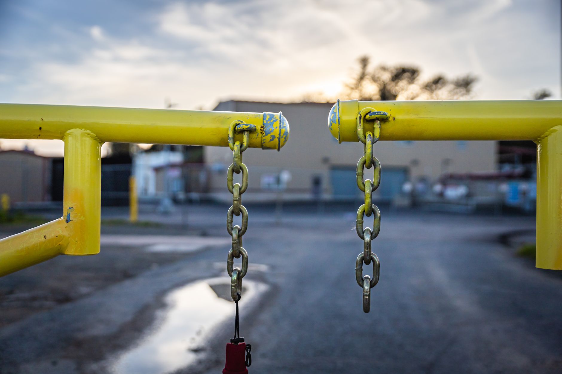 A yellow barrier with chains blocks an industrial road at dusk, symbolizing security and restriction in Austin, TX