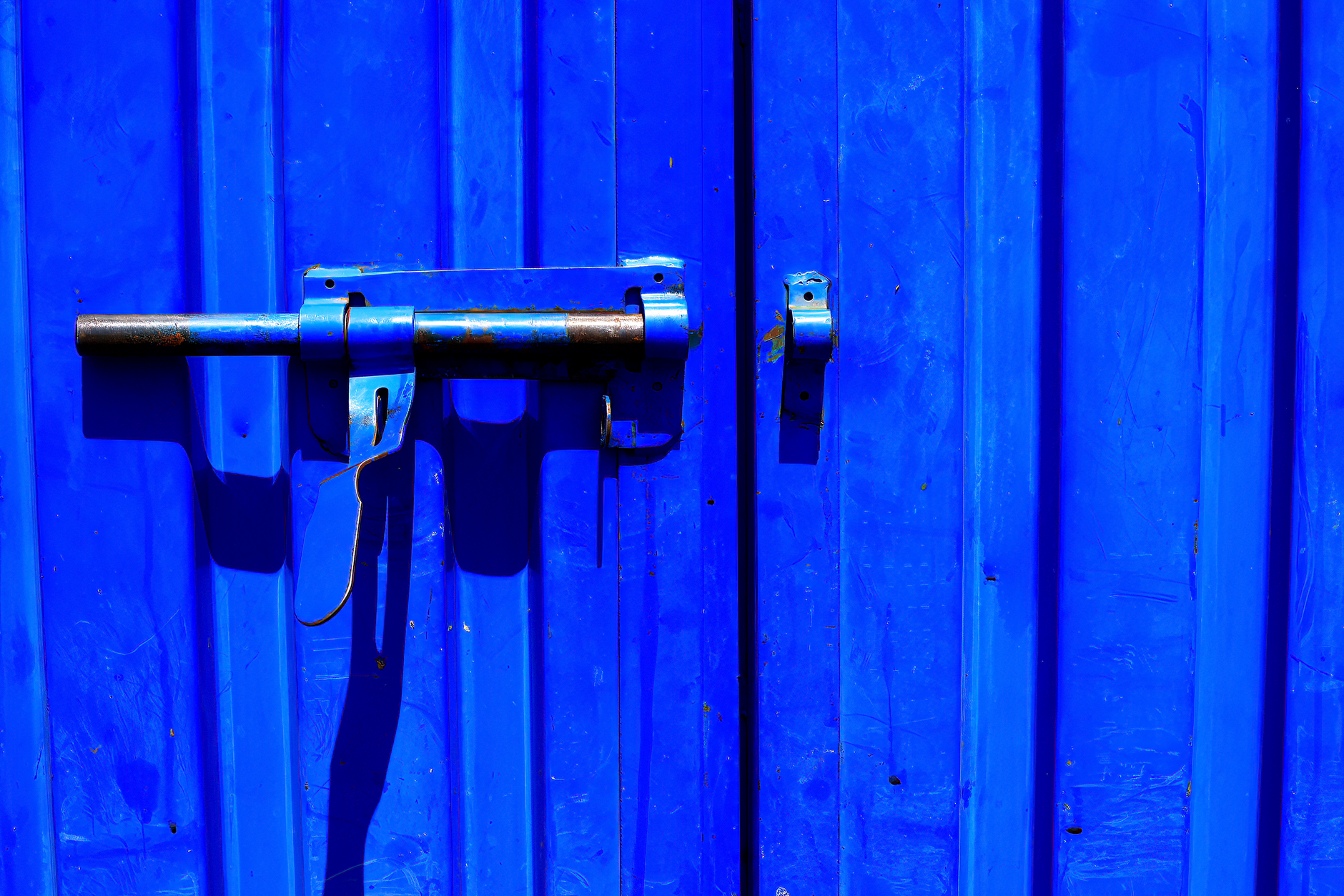 Close-up of a vibrant blue metal door with a rustic lock, casting a dramatic shadow in Austin, TX